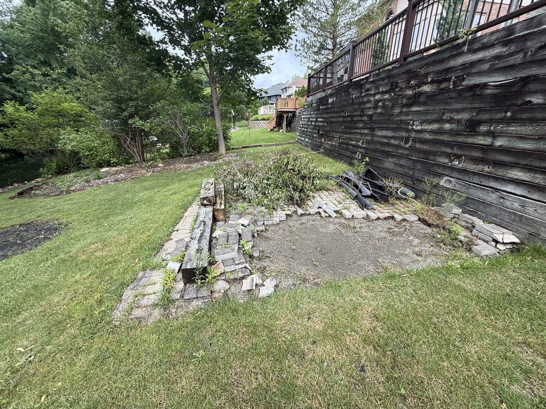 Collapsed paver patio and weeds along a retaining wall before landscaping